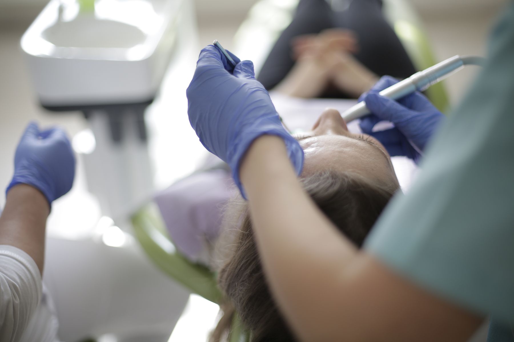 A dentist working chairside with a handpiece and mouth mirror